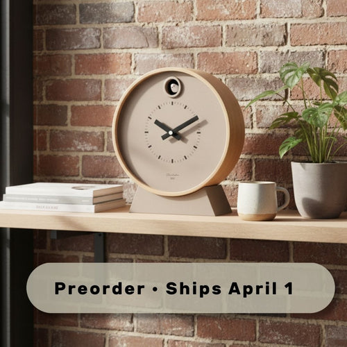Wooden clock on a shelf with a plant and books against a brick wall, preorder text overlay.