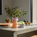 Colorful vase with a plant on a table next to a bowl of fruit