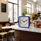 Big Railway Blue Square Kitchen Wall Clock with Dutch Design and Functional Design on a marble café counter next to pastries.