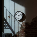 Factory Black XL Clock on a textured wall with sunlight and shadow highlights Dutch Design and Functional Design.