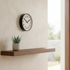 Factory Black XL Clock on textured wall above minimal wooden shelf with potted succulent, Dutch Design functional style