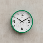 Round wall clock with green frame on a textured beige wall